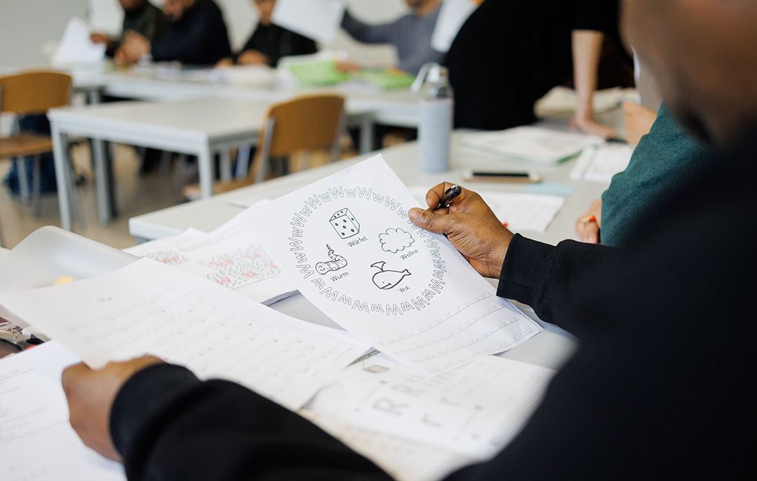 Eine Schülerin hält ein Aufgabenblatt in der Hand, während sie an einem Tisch sitzt.