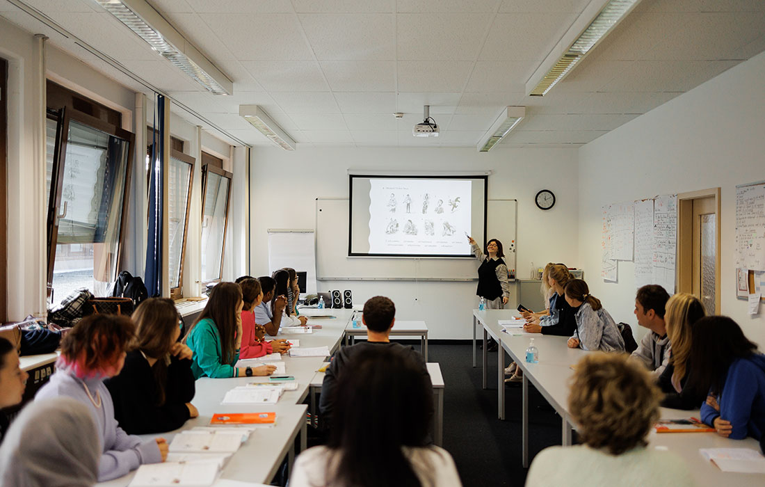 Ein Klassenraum mit Sprachschülern, die Lehrerin steht vorne und zeigt den Schülern etwas auf dem Whiteboard.